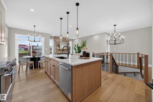 Kitchen island with integrated dishwasher, wood-finish flooring, stone fireplace, and a contemporary open-tread staircase with metal balusters - 209 Hampshire, Sherwood Park, AB 