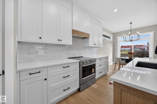 White shaker-style cabinetry with black hardware, white countertops, wood-finish flooring, and a subway tile backsplash - 209 Hampshire, Sherwood Park, AB 
