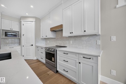 White shaker cabinetry, light-toned wood-finish flooring, stainless steel range, light-toned countertops, and a full tile backsplash - 209 Hampshire, Sherwood Park, AB 