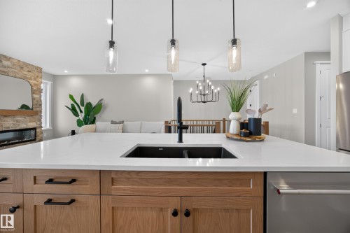 Kitchen island with a built-in sink, stone countertops, wood cabinetry, and pendant lighting - 209 Hampshire, Sherwood Park, AB 