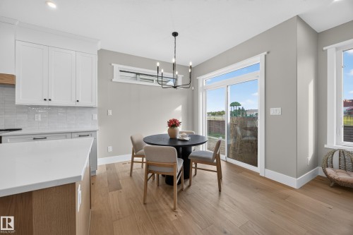 Bright dining area with wood-finish flooring, a sliding glass door, white trim, and a contemporary chandelier - 209 Hampshire, Sherwood Park, AB 