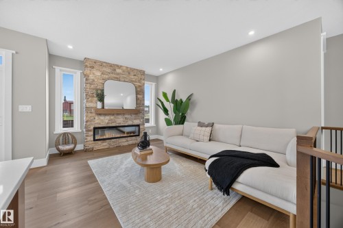 Stone-clad fireplace with an integrated linear firebox, wood-finish flooring, recessed lighting, and expansive windows - 209 Hampshire, Sherwood Park, AB 