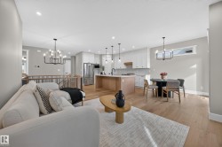 Open-concept living area with wood-finish flooring, a kitchen island, integrated stainless steel appliances, and a modern chandelier - 