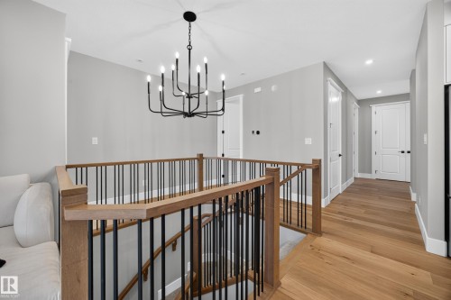 Hardwood flooring, wood-finish railing with black iron spindles, white doors, recessed lighting, and a black chandelier - 209 Hampshire, Sherwood Park, AB 