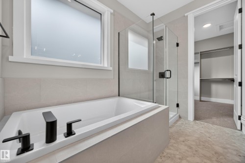 Soaking tub with matte black fixtures, glass-enclosed shower, tiled flooring, and a frosted window - 209 Hampshire, Sherwood Park, AB 