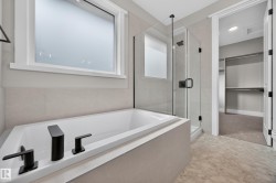 Soaking tub with matte black fixtures, glass-enclosed shower, tiled flooring, and a frosted window - 