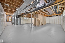 Expansive unfinished basement featuring a painted concrete floor, exposed ceiling joists, insulation, and framing for a separate room - 