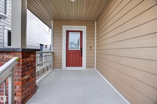 Covered porch featuring a red entry door with glass insert, concrete flooring, brick pillar with dark cap, and horizontal siding - 209 Hampshire, Sherwood Park, AB 