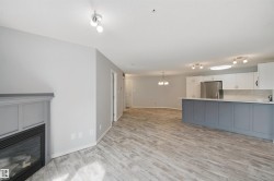 Wood-finish flooring throughout, featuring a built-in fireplace with a paneled surround, white upper cabinetry, a gray island with a countertop, and stainless steel appliances - 