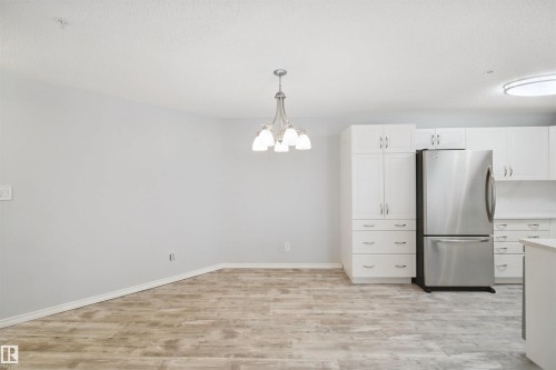 Wood-finish flooring, white cabinetry, stainless steel refrigerator, and a contemporary chandelier - #208 16035 132 St Nw, Edmonton, AB 