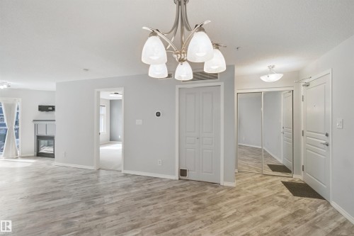 Light wood-finish flooring throughout, modern ceiling light fixture, neutral wall color, and a built-in fireplace - #208 16035 132 St Nw, Edmonton, AB 