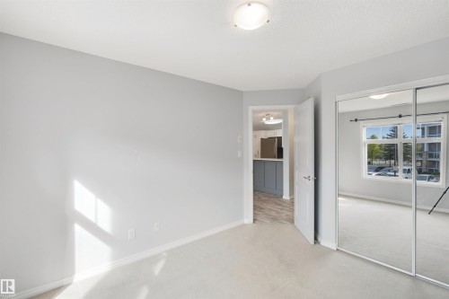 Neutral-toned walls, carpet flooring, mirrored sliding closet doors, and a flush mount ceiling light fixture - #208 16035 132 St Nw, Edmonton, AB 