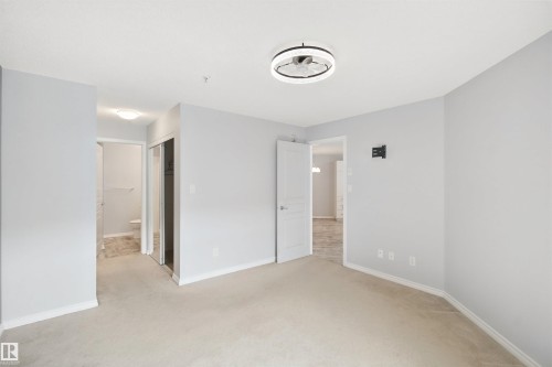 Spacious room with light-toned carpet flooring, a contemporary ceiling light fixture, and a mirrored closet door - #208 16035 132 St Nw, Edmonton, AB 