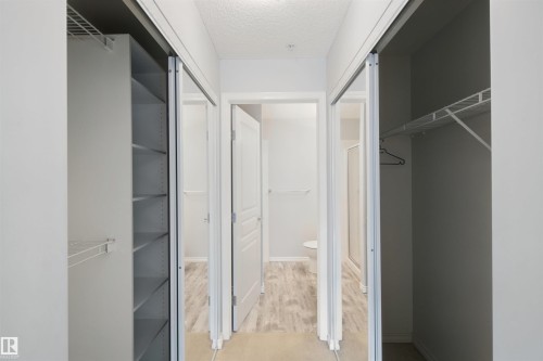 Sliding closet doors with shelving, wire rack storage, and wood-finish flooring - #208 16035 132 St Nw, Edmonton, AB 
