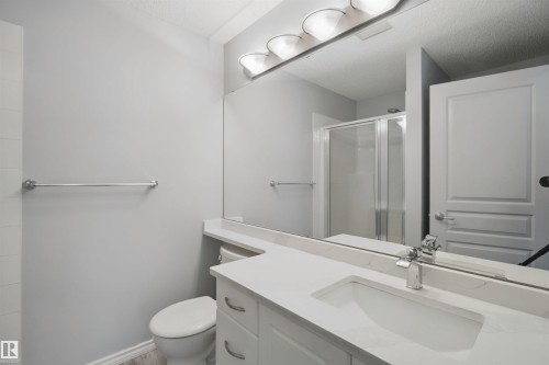 Vanity with an integrated sink, polished chrome faucet, expansive wall-mounted mirror, and overhead vanity lighting - #208 16035 132 St Nw, Edmonton, AB 