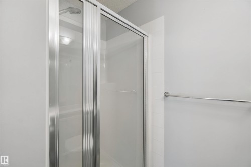 Shower enclosure with sliding glass doors, chrome hardware, and a white tiled surround - #208 16035 132 St Nw, Edmonton, AB 