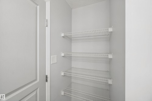 Built-in wire shelving within a storage closet, featuring light gray wall paint and white trim details - #208 16035 132 St Nw, Edmonton, AB 