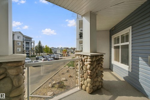 Private balcony with stone-clad columns, glass railing, and concrete flooring - #208 16035 132 St Nw, Edmonton, AB 