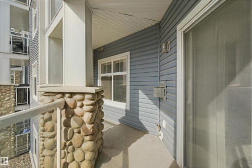 Balcony with river rock column, glass railing, concrete flooring, and sliding glass door access - #208 16035 132 St Nw, Edmonton, AB 