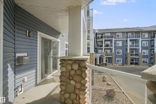 Private balcony featuring a sliding glass door, pebble stone accent columns, and a glass-paneled railing - #208 16035 132 St Nw, Edmonton, AB 