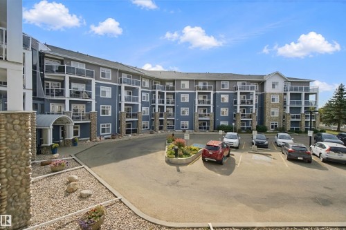 Multi-story residential building with stone and siding exterior, multiple private balconies with glass railings, covered main entrance, and an on-site parking area - #208 16035 132 St Nw, Edmonton, AB 
