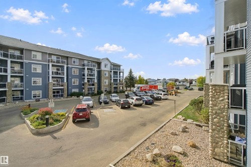 Multi-story building featuring stone accents, private balconies with glass railings, and an expansive paved parking area - #208 16035 132 St Nw, Edmonton, AB 