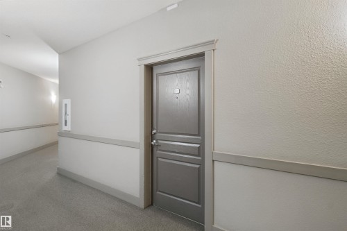 Textured wall finish, panel door with hardware, wall-mounted light fixture, fire extinguisher cabinet, and baseboard trim - #208 16035 132 St Nw, Edmonton, AB 