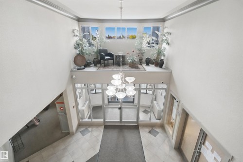 Two-story foyer featuring an overhead chandelier, a glass-paneled entry, and a second-level landing with multiple windows - #208 16035 132 St Nw, Edmonton, AB 