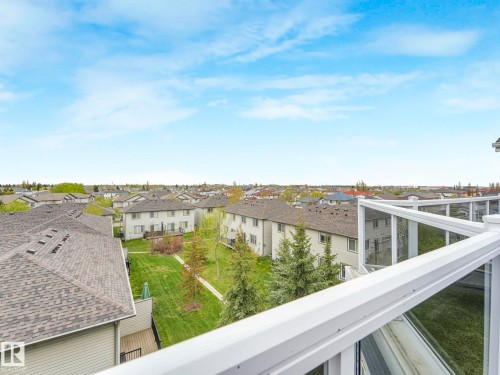 White railing with glass panels overlooking residential neighborhood roofs and green spaces - #208 16035 132 St Nw, Edmonton, AB 
