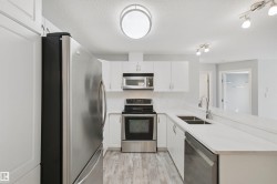 Kitchen featuring stainless steel appliances, white cabinetry, a double basin sink, and wood-finish flooring - 