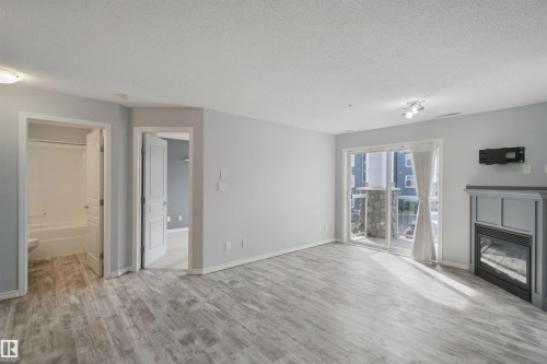 Wood-finish flooring throughout, sliding glass door leading to a balcony, modern fireplace, and recessed lighting - #208 16035 132 St Nw, Edmonton, AB 