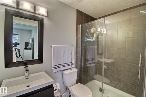 Framed mirror with integrated vanity lighting, contemporary single-handle faucet, glass-enclosed shower, and dark-toned wall tiling - 35 Hudson Cove, Spruce Grove, AB 
