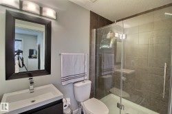 Framed mirror with integrated vanity lighting, contemporary single-handle faucet, glass-enclosed shower, and dark-toned wall tiling - 