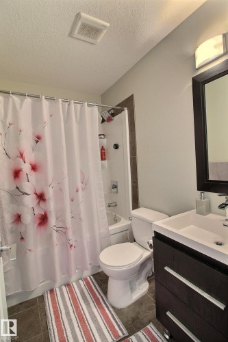Built-in bathtub with shower, white toilet, dark wood-finish vanity with square sink, wall-mounted light fixture, and tile flooring - 35 Hudson Cove, Spruce Grove, AB 