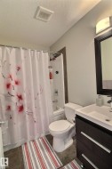 Built-in bathtub with shower, white toilet, dark wood-finish vanity with square sink, wall-mounted light fixture, and tile flooring - 