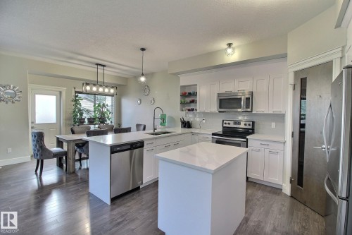 Contemporary kitchen featuring white cabinetry, stainless steel appliances, a center island, and wood-finish flooring - 35 Hudson Cove, Spruce Grove, AB 