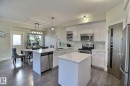 Contemporary kitchen featuring white cabinetry, stainless steel appliances, a center island, and wood-finish flooring - 35 Hudson Cove, Spruce Grove, AB 