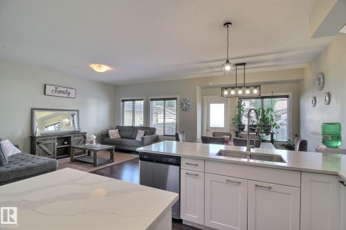 Kitchen island with a double basin stainless steel sink, white shaker cabinetry, stainless steel dishwasher, and light-toned countertops - 35 Hudson Cove, Spruce Grove, AB 