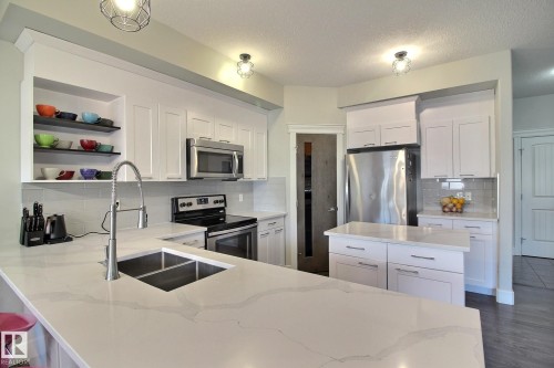 Contemporary kitchen featuring a dual-basin undermount sink, quartz countertops, white cabinetry, stainless steel appliances, and tiled backsplash - 35 Hudson Cove, Spruce Grove, AB 