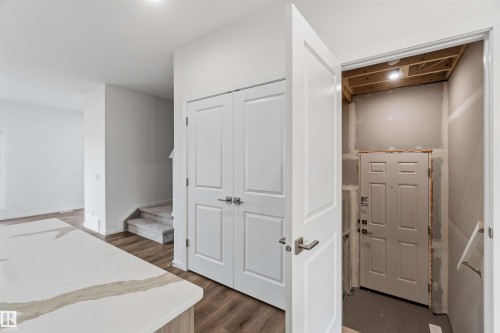 Wood-finish flooring, white paneled doors, and a quartz countertop with veining - 5733 Hawthorn Common Sw, Edmonton, AB 