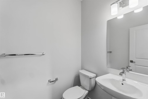 Pedestal sink with chrome faucet, toilet, wall-mounted mirror, and vanity lighting fixture - 5733 Hawthorn Common Sw, Edmonton, AB 