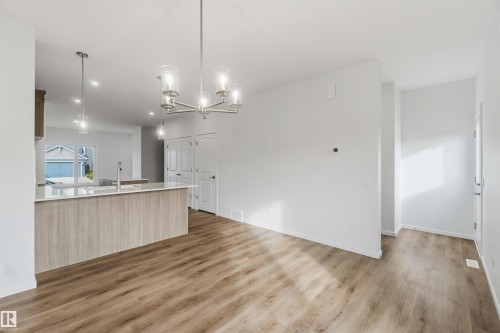Open-concept interior featuring wood-finish flooring, a kitchen island with a light-toned countertop, recessed lighting, and a brushed nickel chandelier - 5733 Hawthorn Common Sw, Edmonton, AB 