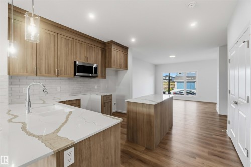 Kitchen featuring light wood-finish cabinetry, white subway tile backsplash, stainless steel microwave, and white countertops with integrated sink - 5733 Hawthorn Common Sw, Edmonton, AB 