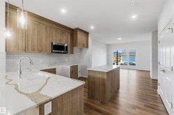 Kitchen featuring light wood-finish cabinetry, white subway tile backsplash, stainless steel microwave, and white countertops with integrated sink - 