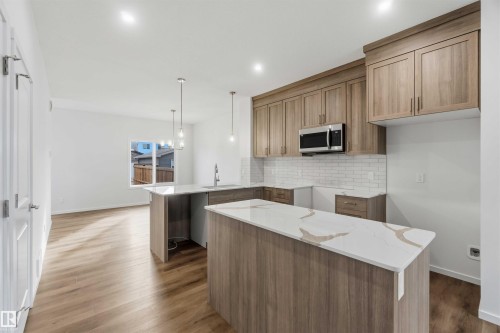 Two-tone kitchen cabinetry, stainless steel microwave, white subway tile backsplash, light wood-finish flooring, and white countertops - 5733 Hawthorn Common Sw, Edmonton, AB 