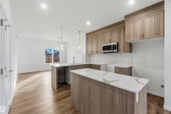 Two-tone kitchen cabinetry, stainless steel microwave, white subway tile backsplash, light wood-finish flooring, and white countertops - 