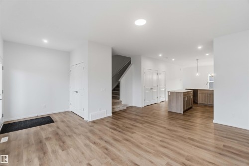 Open-concept living space featuring wood-finish flooring, recessed lighting, white walls, kitchen island, and a staircase with carpeted treads - 5733 Hawthorn Common Sw, Edmonton, AB 