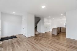 Open-concept living space featuring wood-finish flooring, recessed lighting, white walls, kitchen island, and a staircase with carpeted treads - 