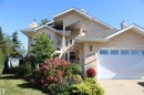 Stucco exterior with a peaked roofline, an attached heated two-car garage with transom windows, a front entry with a decorative light fixture, and established front landscaping - 3815 41 Street Nw, Edmonton, AB 