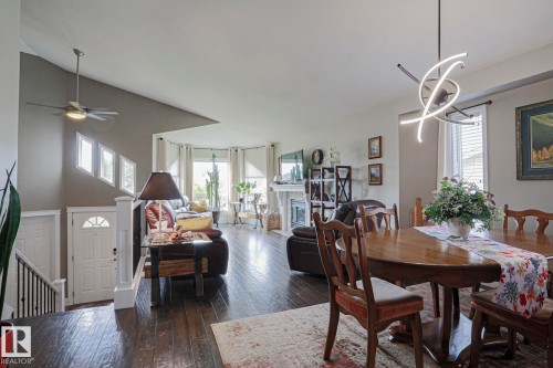 Open-concept living and dining areas with wood-finish flooring, a modern chandelier, a ceiling fan, and a fireplace with a decorative mantel - 3815 41 Street Nw, Edmonton, AB 